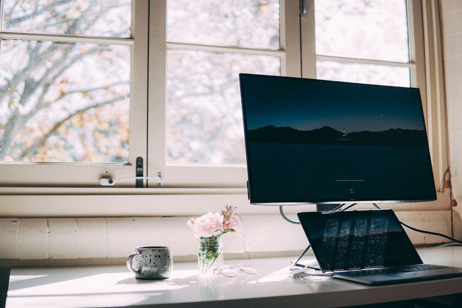 A peaceful home office setup with a desktop and laptop by a window, decorated with flowers and a mug.