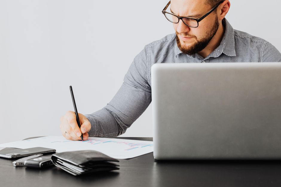 A focused man analyzing financial papers with a laptop in an office setting.